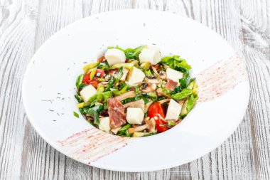 Taze sebze salatası jambon, ıspanak, mantar, domates, peynir, soğan, salatalık ve hafif ahşap arka plan üzerinde plaka üzerinde avokado ile. Sağlıklı gıda. Üstten görünüm