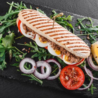 Ton balığı, yumurta, taze sebze ve Yeşiller siyah taş zemin üzerine siyah şeyl gemide ile sandviç. Sağlıklı gıda kavramı. Üstten görünüm, düz yatıyordu