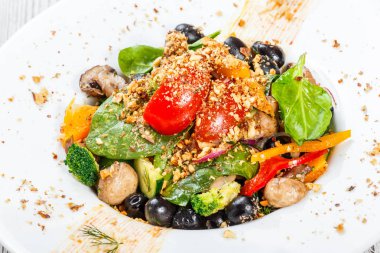 Ispanak, mantar, domates, soğan, salatalık, brokoli, zeytin ve açık ahşap renkli bir tabağa fındık ile sebze salatası. Sağlıklı gıda. Üstten görünüm