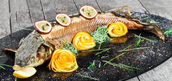 Baked sturgeon fish with rosemary, lemon and passion fruit on plate on wooden background close up. Healthy food. Top view. Russian traditions. Top view