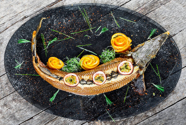 Baked sturgeon fish with rosemary, lemon and passion fruit on plate on wooden background close up. Healthy food. Top view. Russian traditions. Top view