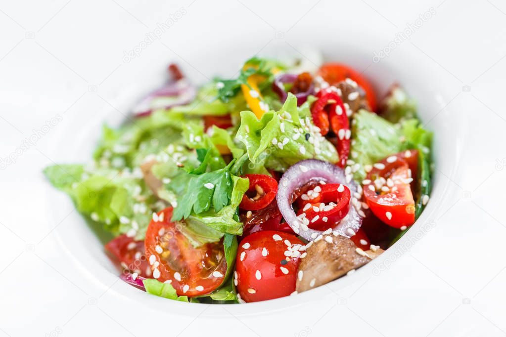 Fresh vegetable salad with lettuce, grilled mushrooms, tomatoes, sweet peppers and sesame seeds on plate on light wooden background close up. Healthy food. Top view