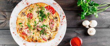 Omlet dilim jambon, mantar, yeşillik, peynir ve domates koyu ahşap zemin üzerinde. Sıcak ve sağlıklı kahvaltı, pizza