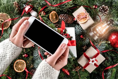 Cep telefonu tutan eller. Noel hediye kutuları kırmızı dekorasyon, çam dalları, çam kozalakları tatil arka plan üzerinde. Noel ve mutlu yeni yıl tema. Düz yatıyordu, en iyi görünümü