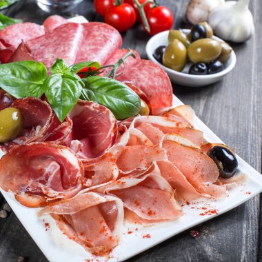 Meze tabağı soğuk et tabağı prosciutto, dilim jambon, salam, zeytin ahşap zemin üzerinde ve fesleğen ile dekore edilmiştir. Etli meze. Üstten görünüm