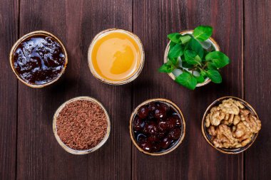 Bölümü bardak koyu ahşap masa, reçel, bal, nane, rendelenmiş çikolata, vişne reçeli, ceviz sağlıklı malzemelerle. Üstten görünüm