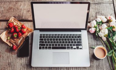 Laptop bilgisayarı kaba ahşap masada kahve fincanı ve şakayık çiçekleri açık hava parkında.
