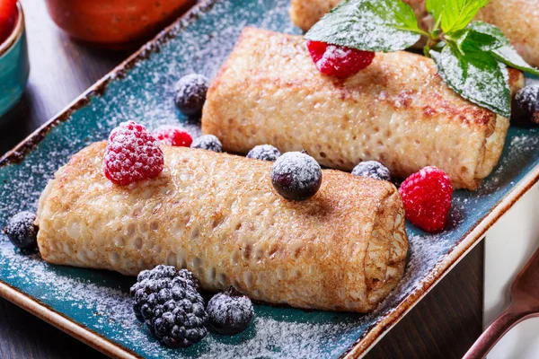 Pancakes with cream cheese, powdered sugar, sour cream and berries on plate close up. Traditional Russian cuisine at the Pancake week or Shrovetide. Flat lay. Top view