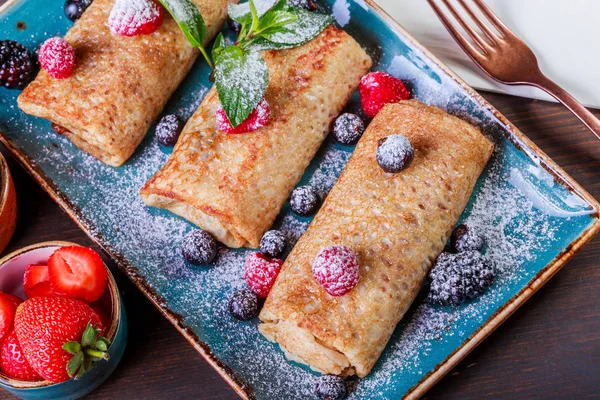 Pancakes with cream cheese, powdered sugar, sour cream and berries on plate close up. Traditional Russian cuisine at the Pancake week or Shrovetide. Flat lay. Top view