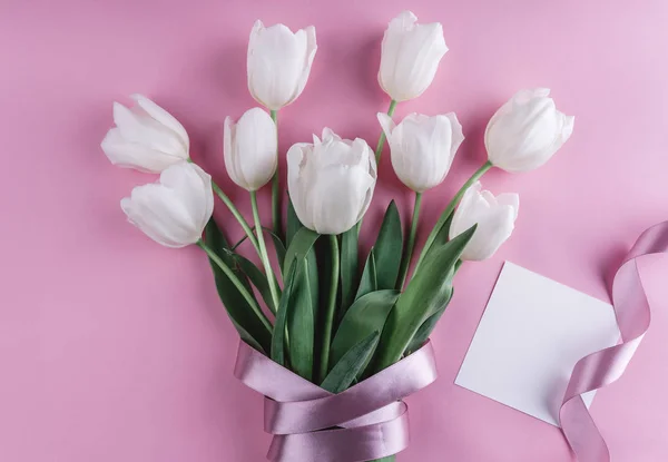 Bouquet of white tulips flowers and sheet of paper over light pink background. Greeting card or wedding invitation. Flat lay, top view, copy space — Stock Image Bouquet White Tulips Flowers Sheet Paper Light Pink Background Greeting Royalty Free Stock Images