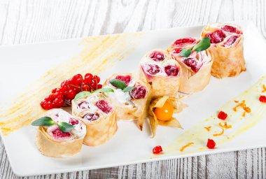 Krem peynirli gözleme, kiraz çilek ve hafif ahşap zemin üzerine physalis tarafından dekore edilmiş kapatmak. Geleneksel Rus yemekleri. Şekerli tatlı. Düz yatıyordu. Üstten görünüm