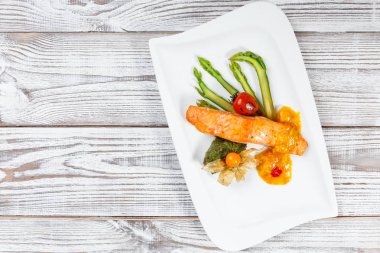 Fırında somon physalis, kuşkonmaz, ahşap arka plan üzerinde otlar ile domates ile süslenmiş. Sıcak balık yemek. Üstten görünüm