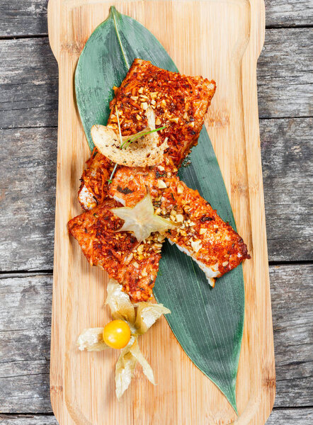 Fried sea fish fillets with physalis and almond on cutting board close up. Hot fish dish