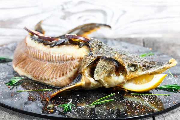 Baked sturgeon fish with rosemary, lemon and passion fruit on plate on wooden background close up. Healthy food. Top view. Russian traditions. Top view