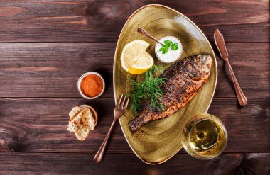 Limon ve Yeşiller ahşap arka plan üzerinde plaka üzerinde ızgara dorado balık. Lezzetli yemek deniz ürünleri. Üstten görünüm