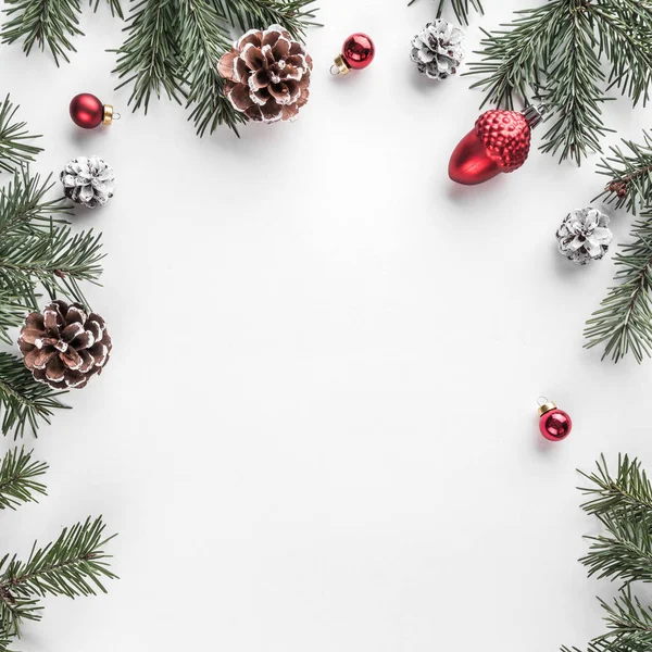 Yaratıcı çerçeve Noel köknar yapılan Beyaz Kağıt arka plan kırmızı süslemeli, çam kozalakları dallarda. Noel ve yeni yıl tema. Düz yatıyordu, en iyi görünümü