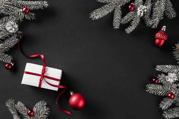 Yaratıcı düzen çerçeve yaptı Noel ağaç dalları, çam kozalakları, koyu arka plan üzerinde kırmızı süslemeli hediyeler. Noel ve yeni yıl tema, kar taneleri. Düz yatıyordu, en iyi görünümü