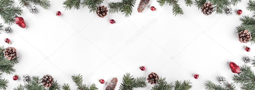 Creative frame made of Christmas fir branches on white background with red decoration, pine cones. Xmas and New Year theme. Flat lay, top view, wide composition