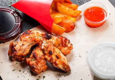 Fırında patates ve Kraft kağıt siyah arka plan üzerine Barbekü sosu ile kızarmış tavuk kanatları. Sıcak et yemekleri. Üstten görünüm 
