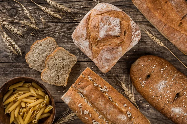 Different fresh bread and flour products pasta on rustic wooden background. Creative layout made of bread. Healthy food concept, top view, flat lay, copy space