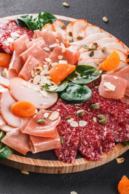 Meze tabağı soğuk et, salam, dilim jambon, kurutulmuş et, salam, et ve kesme tahtası siyah taş zemin üzerine fındık. Et iştah açıcı, gıda kavramı karşılayan