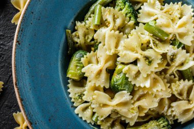 Vegan Farfalle makarna ıspanak soslu brokoli, Brüksel lahanası, plaka karanlık taş zemin üzerine yeşil fasulye ile. Üstten görünüm, düz yatıyordu. Vejetaryen yiyecekler