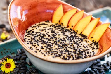 Ayçiçeği tohumu, susam ve parlak ahşap masa üzerinde şeftali ile yulaf lapası. Seçici odak. Sağlıklı Kahvaltı, vegan gıda