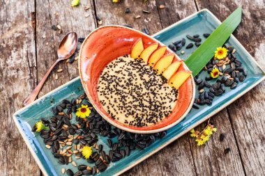 Ayçiçeği tohumu, susam ve parlak ahşap masa üzerinde şeftali ile yulaf lapası. Seçici odak. Sağlıklı Kahvaltı, vegan gıda. Üstten görünüm