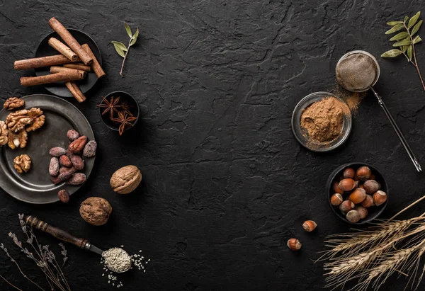 Mix of nuts and spices for baking cakes in bowl and spoon, cinnamon, star anise, hazelnuts, walnuts, wheat, lavender on dark stone table. Organic food, top view, space for text