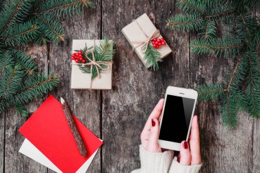 Noel hediyeleri ile ahşap arka plan üzerinde cep telefonu tutan eller, çam dalları. Noel ve mutlu yeni yıl kompozisyon. Düz yatıyordu, en iyi görünümü