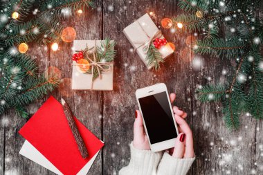 Noel hediyeleri ile ahşap arka plan üzerinde cep telefonu tutan eller, çam dalları. Noel ve mutlu yeni yıl kompozisyon. Düz yatıyordu, en iyi görünümü