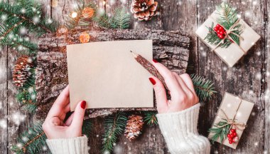 Noel hediyeleri, kabuk dokusu, çam dalları, çam kozalakları, kırmızı süslemeleri ile ahşap arka plan üzerinde Noel Baba'ya bir mektup yazma el. Noel ve mutlu yeni yıl kartı. Düz yatıyordu, en iyi görünümü
