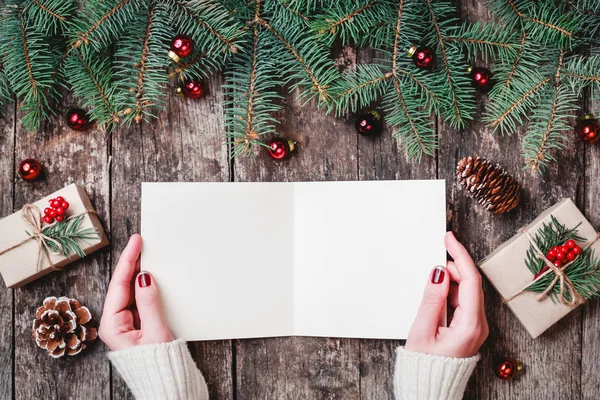 女性の手を書くと木製の背景にクリスマス プレゼント モミの枝 お菓子をサンタさんへ手紙を読みます クリスマスと新年のカード フラット横たわっていた トップ ビュー — ストック写真