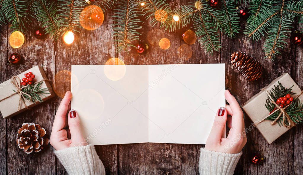 Female hand writing and reading a letter to Santa on wooden background with Christmas gifts, Fir branches and candy. Xmas and Happy New Year card. Flat lay, top view