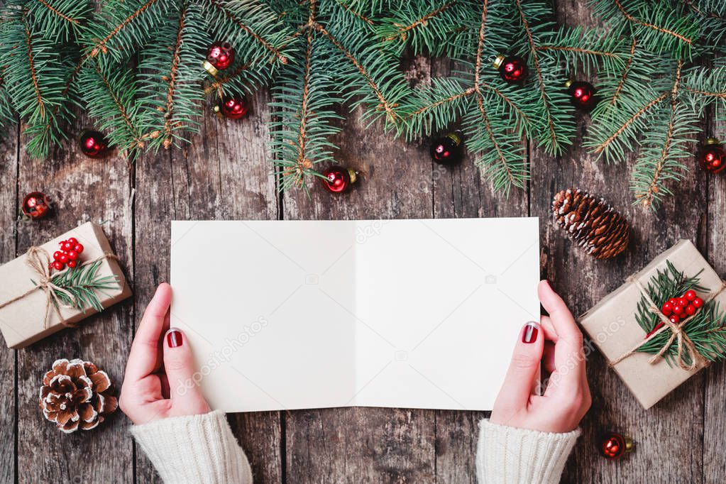 Female hand writing and reading a letter to Santa on wooden background with Christmas gifts, Fir branches and candy. Xmas and Happy New Year card. Flat lay, top view