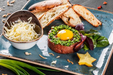 Biftek tartare bir yumurta sarısı, doğranmış yeşil soğan, kızarmış ekmek ve tereyağı karanlık taş zemin üzerine plaka ile devam eder. Yeme sağlıklı gıda kavramı temiz