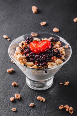 Lezzetli granola yoğurt, taze çilek, çilek cam siyah arka plan ile. Sağlıklı kahvaltı malzemeler. Yeme, vegan gıda kavramı temiz. Üstten görünüm