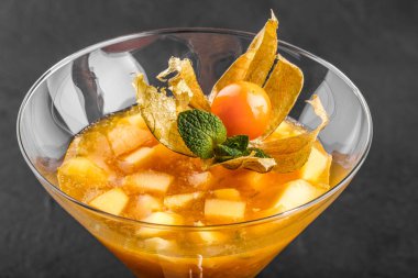 Mango ve Şeftali meyve jöle nane ve karanlık taş zemin üzerine bir bardak physalis süslenmiş. Yaz tatlı