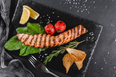 Ispanak, limon, plaka üzerinde otlar ile süslenmiş ahşap arka plan üzerinde ızgara somon fileto. Sıcak balık yemek. Üstten görünüm, düz yatıyordu