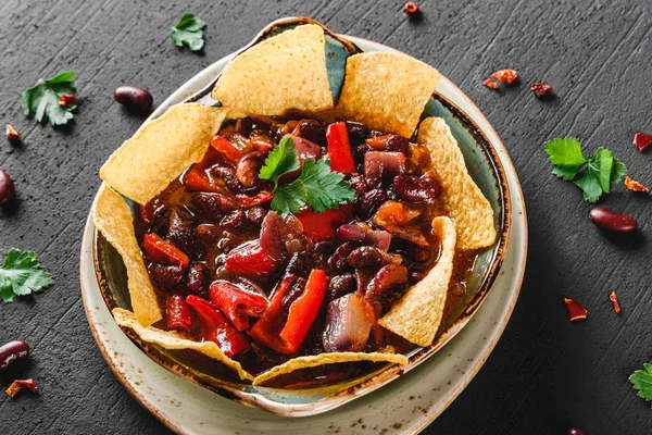 Red bean with nachos or pita chips, pepper and greens on plate over dark background. Mexican snack, Vegetarian food, top view, flat lay, copy space