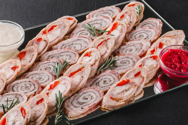 Assorted meat, stuffed chicken roll, meat roll with pepper, greens on black shale background. Meat appetizer, food concept. Top view, flat lay