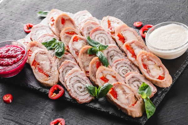 Assorted meat, stuffed chicken roll, meat roll with pepper, greens on black shale background. Meat appetizer, food concept. Top view, flat lay