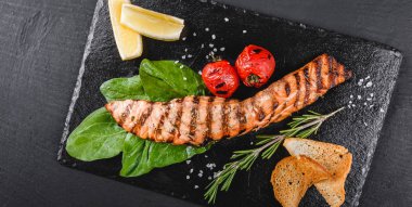 Ispanak, limon, plaka üzerinde otlar ile süslenmiş ahşap arka plan üzerinde ızgara somon fileto. Sıcak balık yemek. Üstten görünüm, düz yatıyordu