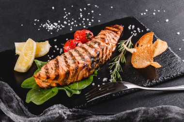 Ispanak, limon, plaka üzerinde otlar ile süslenmiş ahşap arka plan üzerinde ızgara somon fileto. Sıcak balık yemek. Üstten görünüm, düz yatıyordu