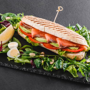 Sandviç kırmızı balık, yumurta, avokado, taze sebze ve Yeşiller siyah taş zemin üzerine siyah şeyl gemide. Sağlıklı gıda kavramı