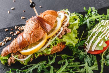 Ton balığı, avokado, taze roka ve Yeşiller siyah taş zemin üzerine siyah şeyl gemide sandviç. Sağlıklı gıda kavramı