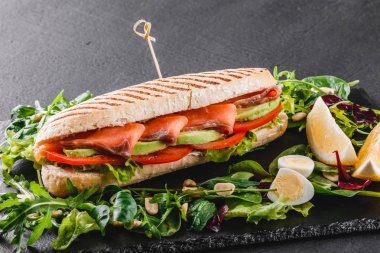 Sandviç kırmızı balık, yumurta, avokado, taze sebze ve Yeşiller siyah taş zemin üzerine siyah şeyl gemide. Sağlıklı gıda kavramı