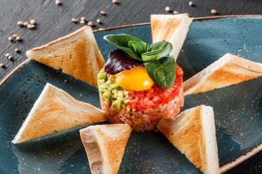 Biftek tartare bir yumurta sarısı, doğranmış avokado, domates ve tost karanlık taş zemin üzerine plaka ile devam eder. Yeme sağlıklı gıda kavramı temiz