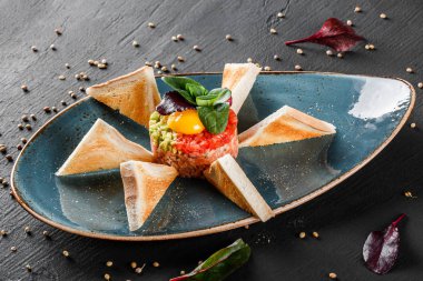 Biftek tartare bir yumurta sarısı, doğranmış avokado, domates ve tost karanlık taş zemin üzerine plaka ile devam eder. Yeme sağlıklı gıda kavramı temiz