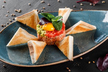 Biftek tartare bir yumurta sarısı, doğranmış avokado, domates ve tost karanlık taş zemin üzerine plaka ile devam eder. Yeme sağlıklı gıda kavramı temiz